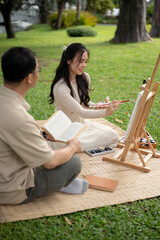 A happy Asian daughter and father are enjoying picnicking in a green park on the weekend together.