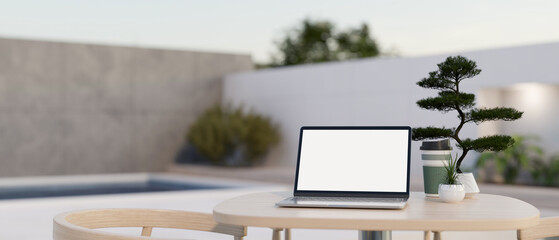 A white-screen laptop mockup on a table in a modern outdoor lounge on a rooftop.