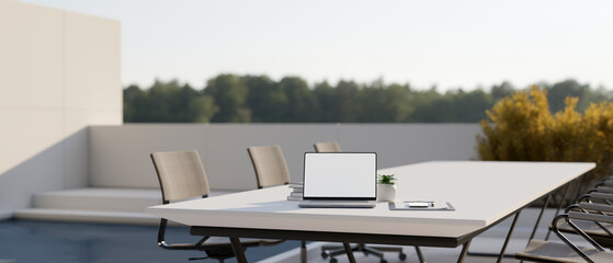 Fototapeta na wymiar A white-screen laptop mockup on a meeting table in a modern outdoor rooftop space.