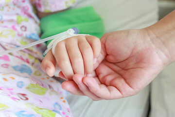 Mother holding child hand with saline IV solution in hospital