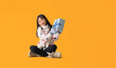 Portrait of cheerful happy Asian little girl wearing Christmas sweater costume, Sitting on floor...