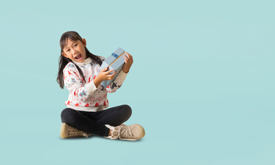 Portrait of cheerful happy Asian little girl wearing Christmas sweater costume, Sitting on floor hands holding xmas gift box happy new year, full body isolated on pastel plain light blue background