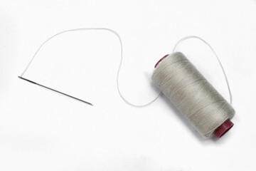 Grey thread and needle over white