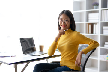 Happy young Asian woman smiling while working with laptop in office.
