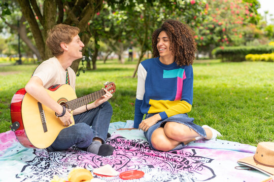 Multi-ethnic couple playing the guitar in a park