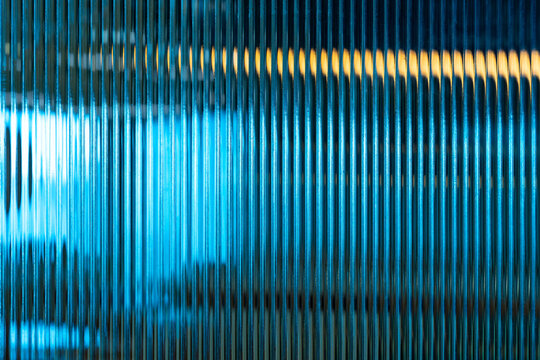 Abstract creative image on patterned glass show vertical lines pattern repetition blurry background of wavy illuminated multi-colored interior soft lighting.glass surface used for artistic backdrop.