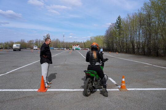 A young woman is learning to ride a motorbike in a motorcycle school. She is taught by a teacher