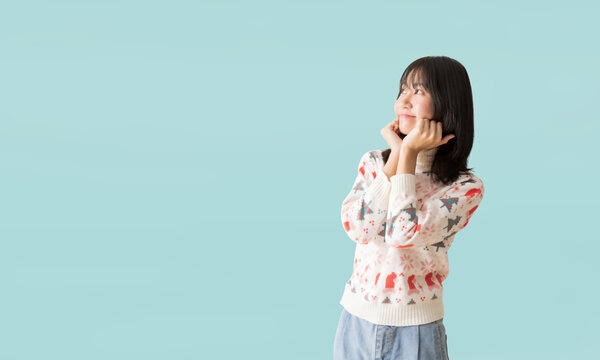Cheerful young Asian teenager girl wearing a Christmas sweater, Happy smiling standing with Looking surprise posing, isolated on pastel plain light blue background