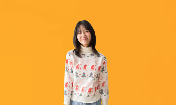 Cheerful young Asian teenager girl wearing a Christmas sweater, Happy smiling standing Looking posing, isolated on yellow background