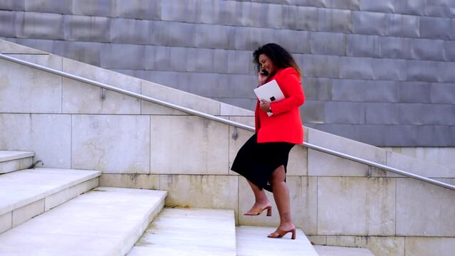 African American confident businesswoman walking on stairs. Black curvy woman talking on phone outdoors. Female empowerment concept.