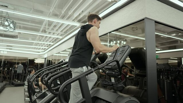 Mature Bearded Muscular Man Doing Cardio on Stair Climber Machine in Fitness Center - low angle