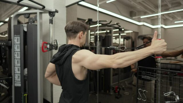 Fitness Trainer Man Training Rear Deltoid Performing Rear Delt Cable Fly Exercise Standing in Front of Mirror. Shoulder Workout