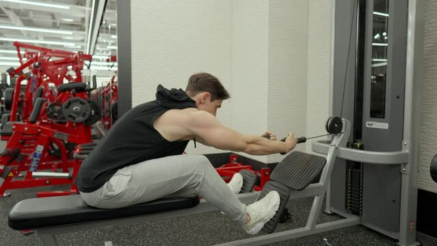 Muscular Man Train Lower Back in Seated Row Cable Machine in Modern Fitness Center