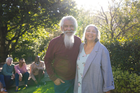 Happy biracial couple of senior friends embracing and smiling in sunny garden