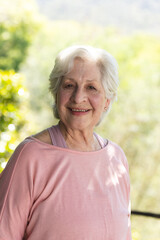 Portrait of happy caucasian senior woman standing and smiling in sunny garden, copy space
