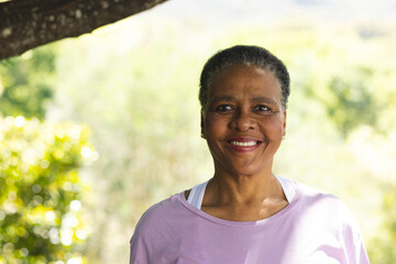 Happy african american senior woman standing and smiling in sunny garden, copy space