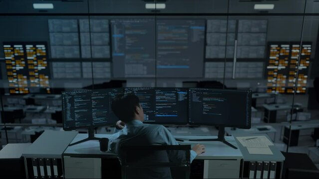 Back View Of Bored Asian Man Developer Write Code With Multiple Computer Screens In The Office
