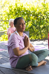 Fototapeta na wymiar Focused african american senior woman practising yoga with friends in sunny garden, copy space