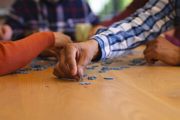 Obraz premium Hands of diverse group of senior friends playing with jigsaw puzzles in sunny dining room at home