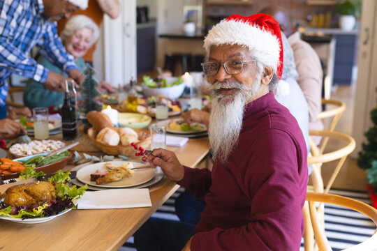 Happy biracial senior man celebrating with friends at christmas dinner in sunny dining room
