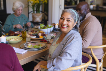 Happy biracial senior woman celebrating with friends at christmas dinner in sunny dining room