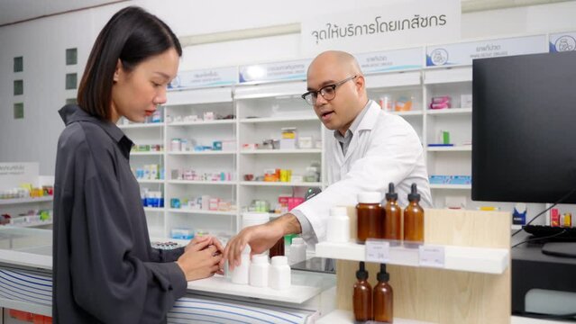 Medical pharmacy and healthcare. Handsome asian male pharmacist wearing lab coat using barcode scanner for selling medicine to customer under prescription order in the pharmacy drugstore.