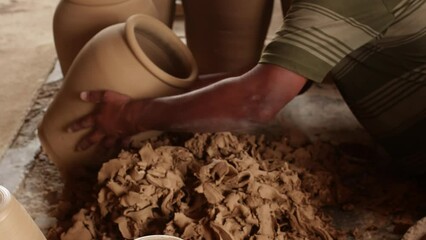 Potter cleaning excess clay before moulding wet clay. Male artist shaping pot with hands on spinning wheel. He is dedicated while working at workplace.