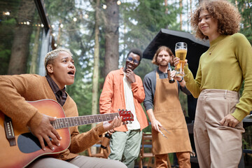 Group of young friends playing guitar and drinking beer at picnic in the forest