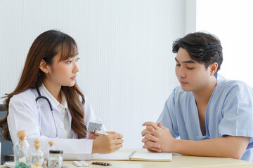 Female doctor and young male patient while consult and explain. Doctor and patient sitting together at table in examination room.
