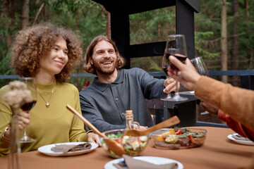 Happy young friends drinking wine at barbecue party while sitting at table outdoors