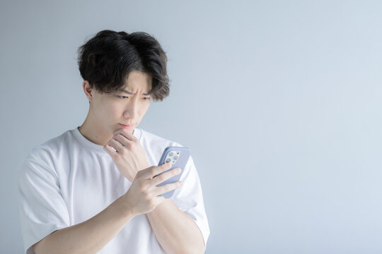 スマホを持つ悩むハンサムな男性 どうしようかな～