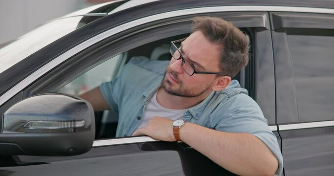 Sad angry man sitting in a car in a traffic jam and gesticulating angrily in impatience and irritation
