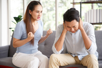 Young asian couple mad at each other in their home. Disgruntled man sitting on couch with his girlfriend which screaming and quarrels with him at home.