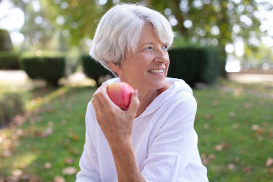 happy mature woman sitting in the meadow eating an apple