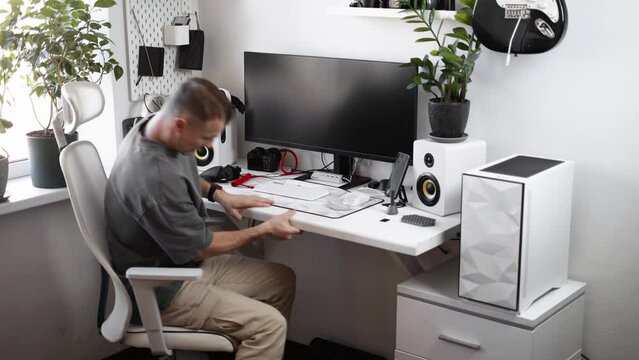 A male photographer sits down at a comfortable workplace in a home office and prepares to get to work. Studio in white tones.