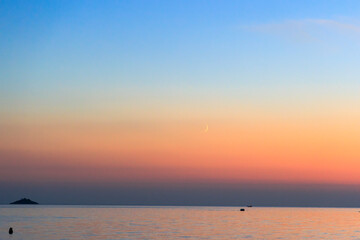 Fototapeta na wymiar Fishing boats sail across the sea near Rovinj in Croatia at dusk while a narrow crescent of the waxing moon is in the sky