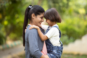 Happy indian Loving mother playing with daughter by carrying at park - concept of family bonding,...