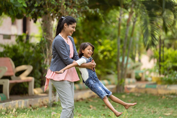 focus on mother, Cheerful indian mother playing by rotating his daughter at park - concept of...
