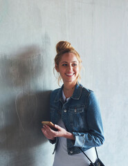 Phone, thinking and smile with a woman student leaning against a gray wall on the campus of her university. Education, idea and mobile with a happy young female pupil standing at college for learning