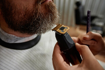 Close-up of barber using shaver to shave beard of customer