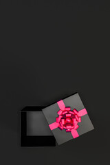 Top view of open black gift box with red ribbon and bow isolated on black background and copy space, vertical format.