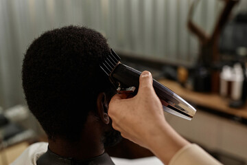 Rear view of customer sitting in chair while barber using trimmer to cut hair