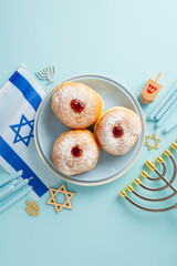 Commemorate Hanukkah traditions through a top-view vertical photo of sufganiyot, Star of David, Israel flag, menorah candle holder, dreidel on pastel blue backdrop, designed for advertisements