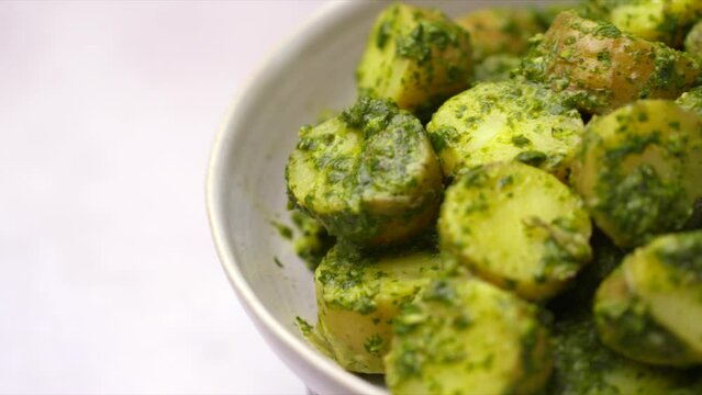 Potato salad with salsa verde. An HD image panning across a white bowl of potatoes dressed in a herb sauce. Shallow Depth of field shot of vegetables.
