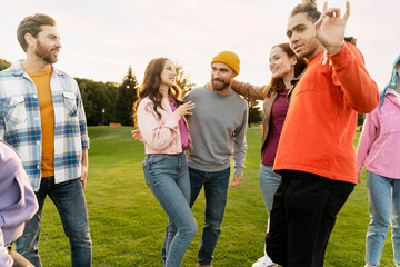 Group of smiling stylish multiracial friends , students wearing colorful clothing laughing, talking, having fun, hangout on corporate party in park. Diversity, friendship, positive lifestyle concept