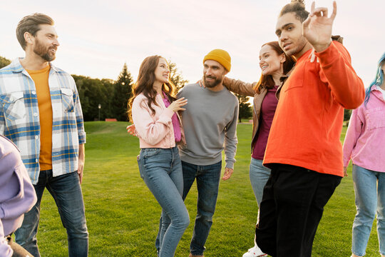 Group of smiling stylish multiracial friends , students wearing colorful clothing laughing, talking, having fun, hangout on corporate party in park. Diversity, friendship, positive lifestyle concept