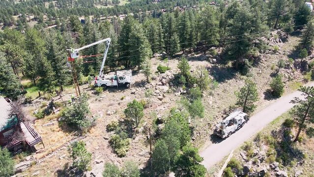 Aerial view of a utility crew using a bucket truck to work on a power pole in a remote mountain neighborhood.