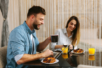 Fototapeta na wymiar Young couple is having breakfast and using a laptop