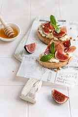 Ricotta, figs, prosciutto and honey bruschetta. Open sandwiches, toasts with cream cheese, fresh figs, Parma ham and basil. Tasty morning breakfast, antipasti or appetizer. Healthy eating. Vertical