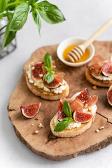 Tasty bruschetta with ciabatta baguette, Parma ham or prosciutto, cream cheese, figs, basil, honey and walnut on wooden board on white background. Antipasti. Vertical, close up. Canape, sandwiches
